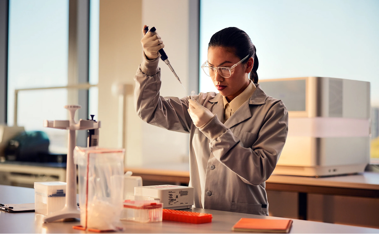 Female scientist, front view, holding tube and pipetting clear liquid, NextSeq 1000/2000 in background