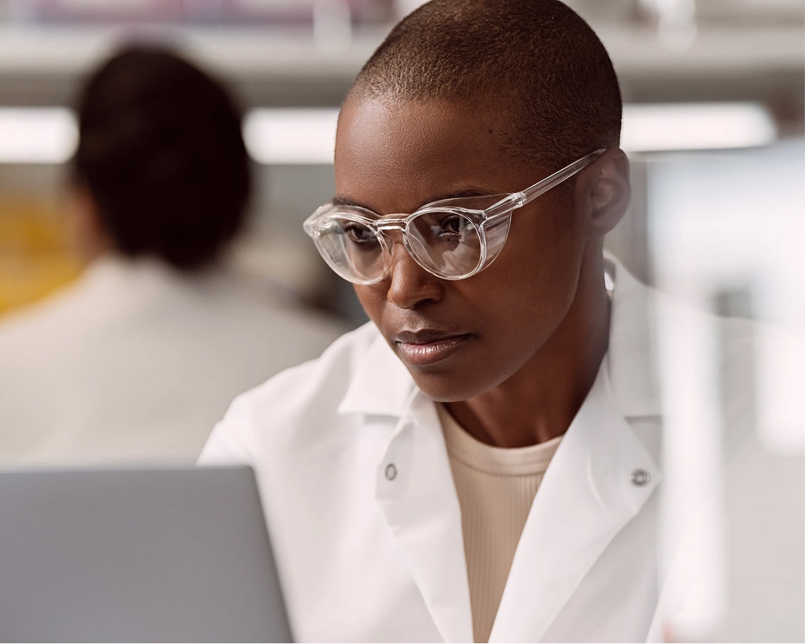 Female scientist analyzing a monitor on a laptop in a lab setting; blurry image of a scientist in the background.