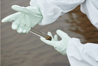 Researcher collecting wastewater sample for testing.