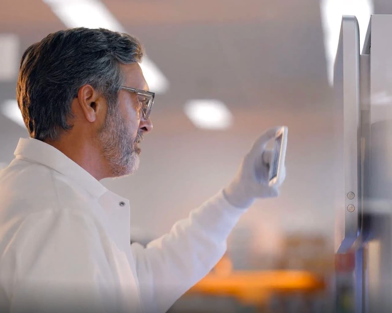 Profile picture of a single male scientist holding up a flow cell in front of his face and inspecting it.