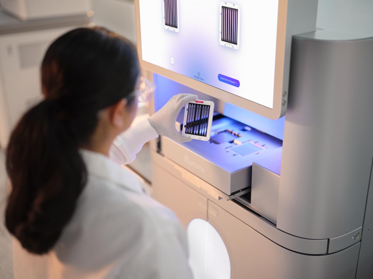 Back view of a female scientist examining a second 25B flow cell cartridge before inserting into a NovaSeq X drawer.