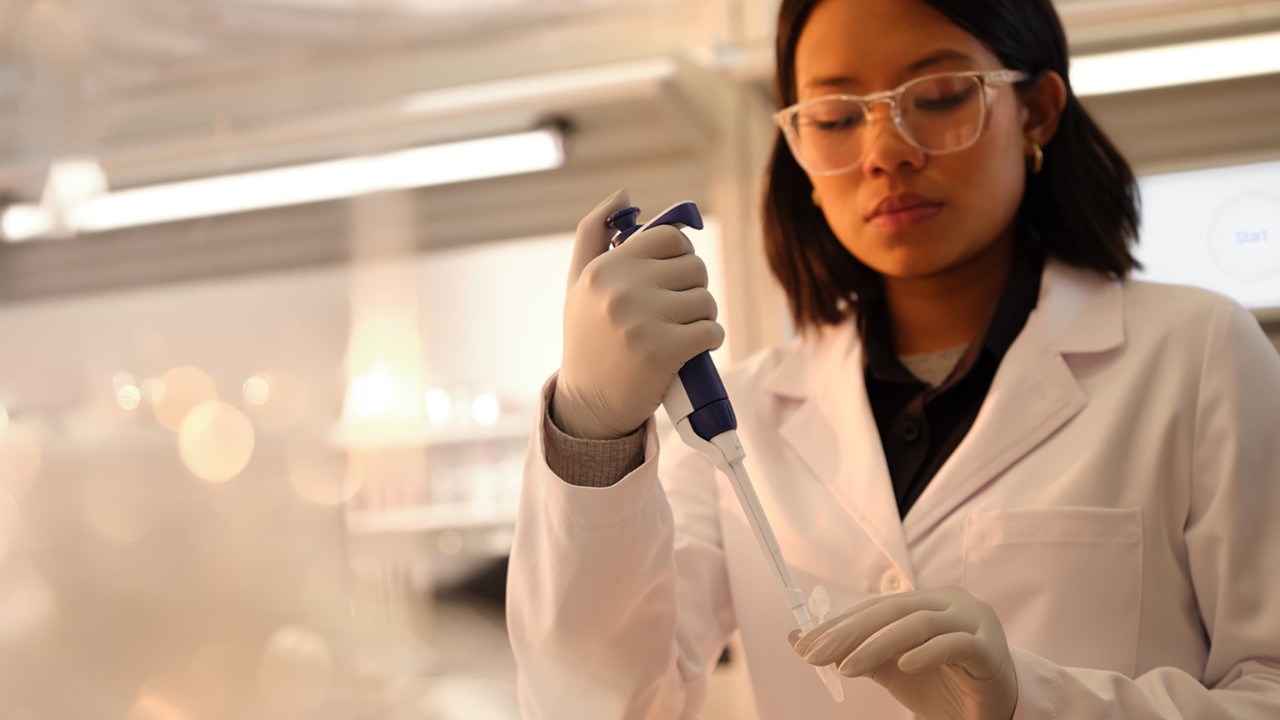 Front view of a female scientist holding a tube in one hand and single pipette in the other, preparing the flow cell for load.