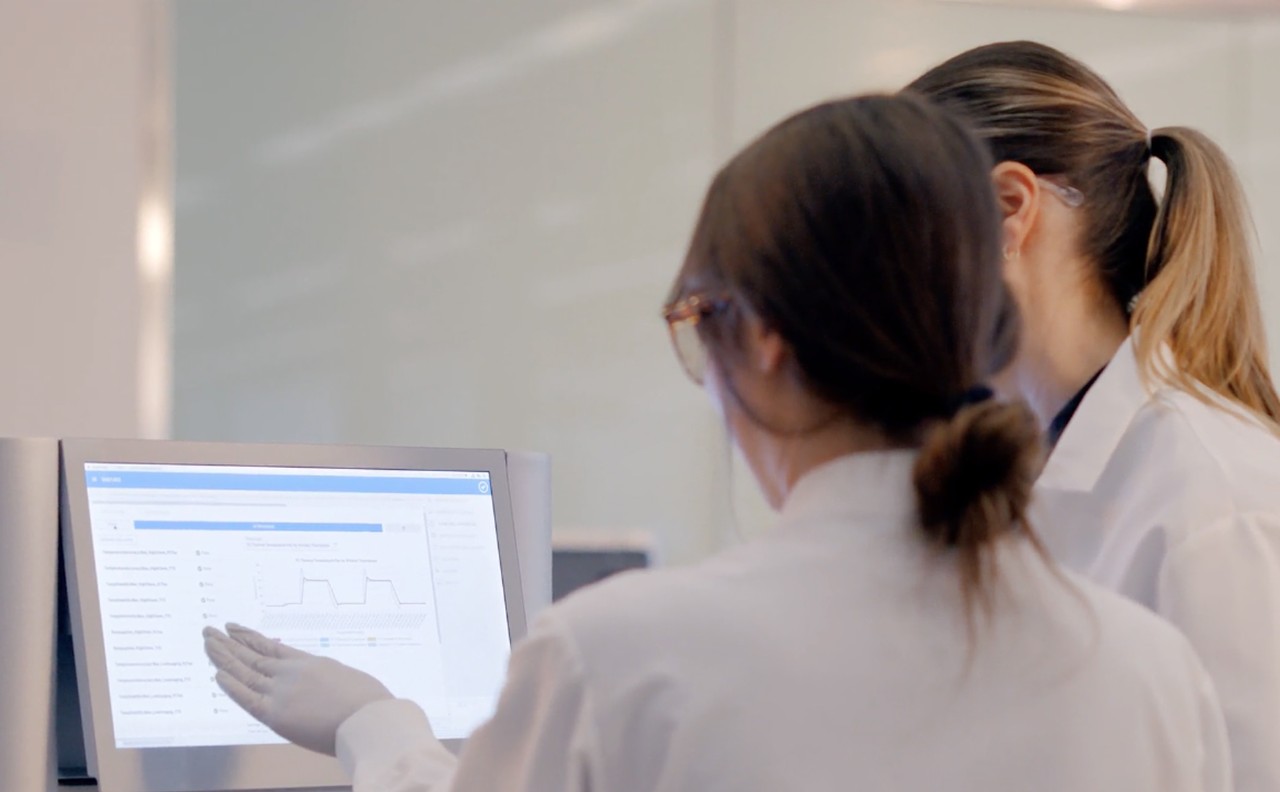 Close up clip of the back of two female scientists discussing results on the monitor of a NextSeq 1000/2000 sequencer, one woman explaining while the other nods.