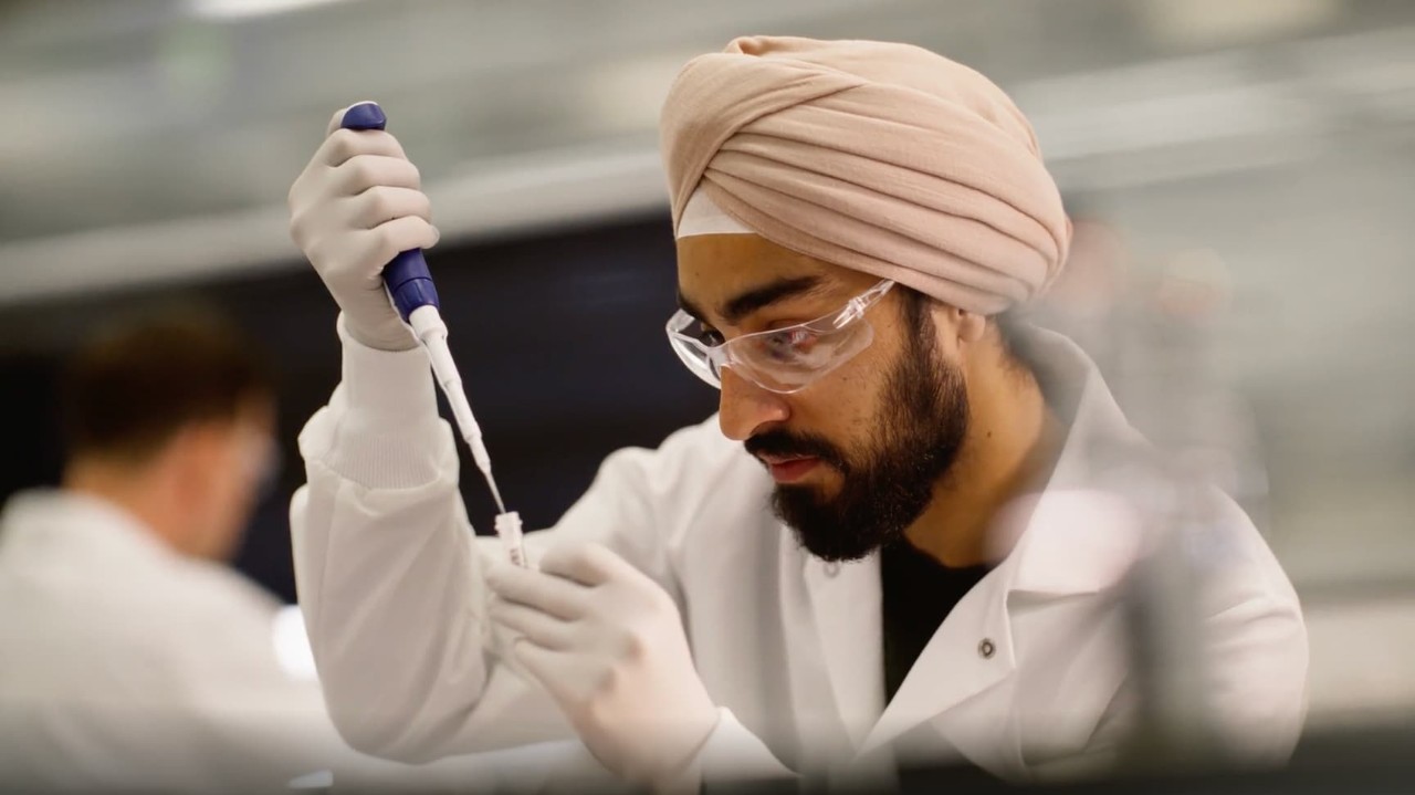 Front view of a male scientist holding the tip of a single pipette in a tube then pulling it out while setting the tube down.