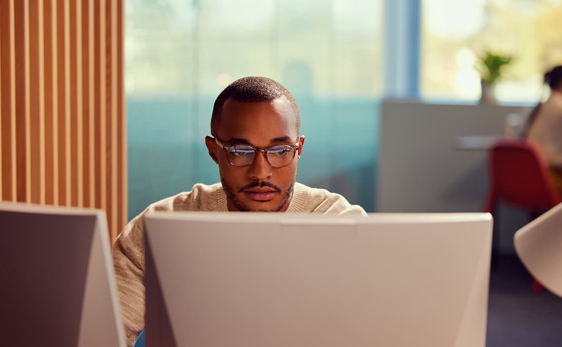 Male analyst, front view, sitting in front of computer screen, partial view of other analyst blurry in the background